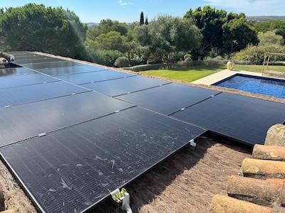 Solar panels installed on a rooftop with a background of trees and a swimming pool under clear skies.