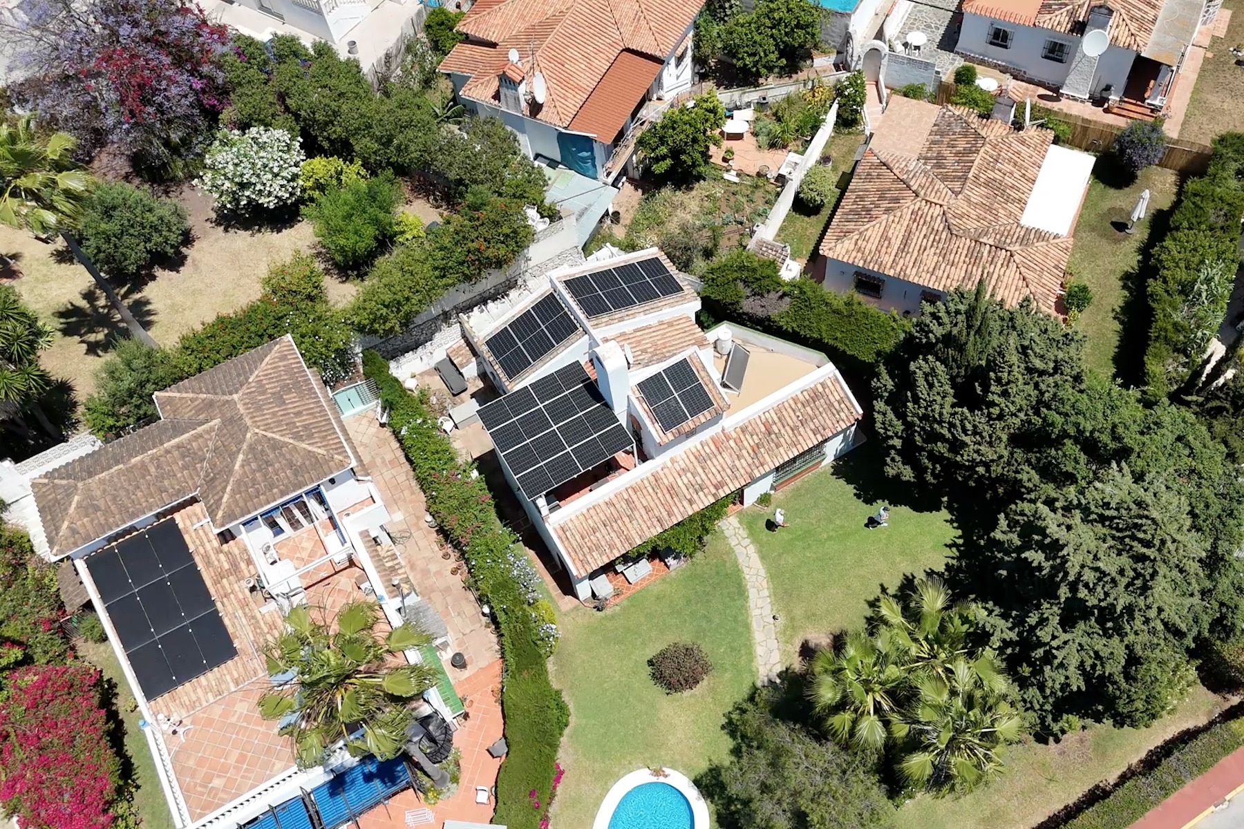 Aerial view of a house with solar panels on the roof, surrounded by a garden and a swimming pool.