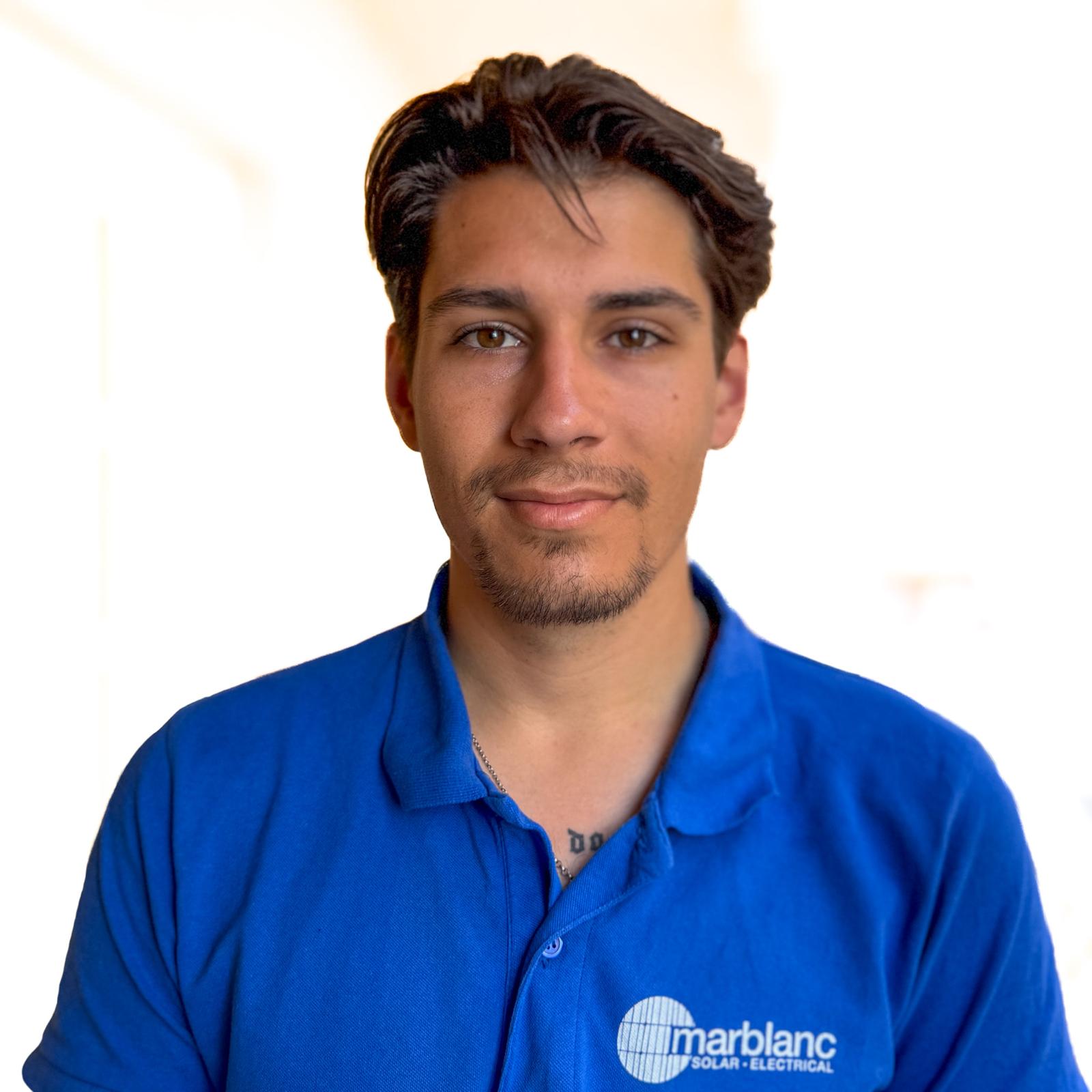 Retrato de un joven con el pelo corto y castaño que lleva un polo azul sobre fondo blanco.