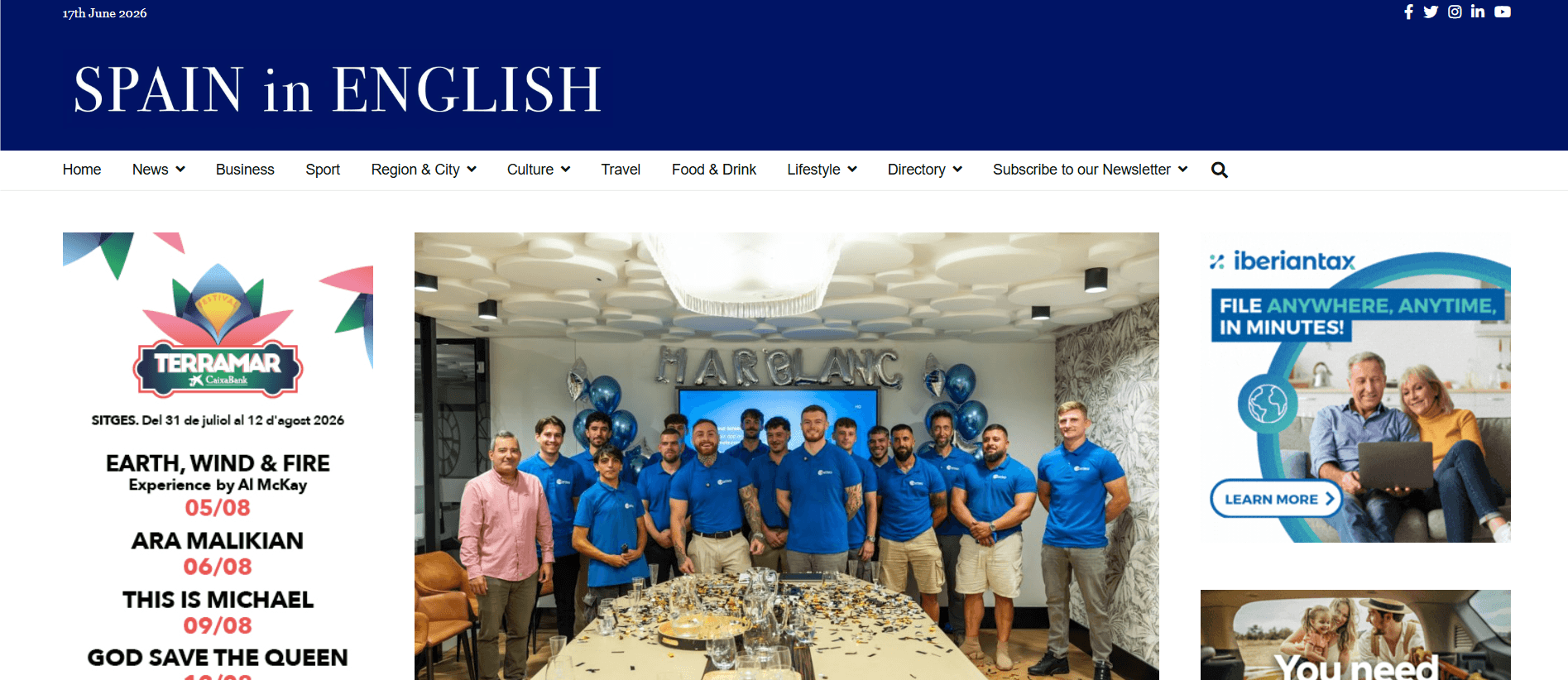 Grupo de personas con polos azules posando para una foto alrededor de una mesa larga cubierta de confeti en un evento de celebración en un salón moderno.
